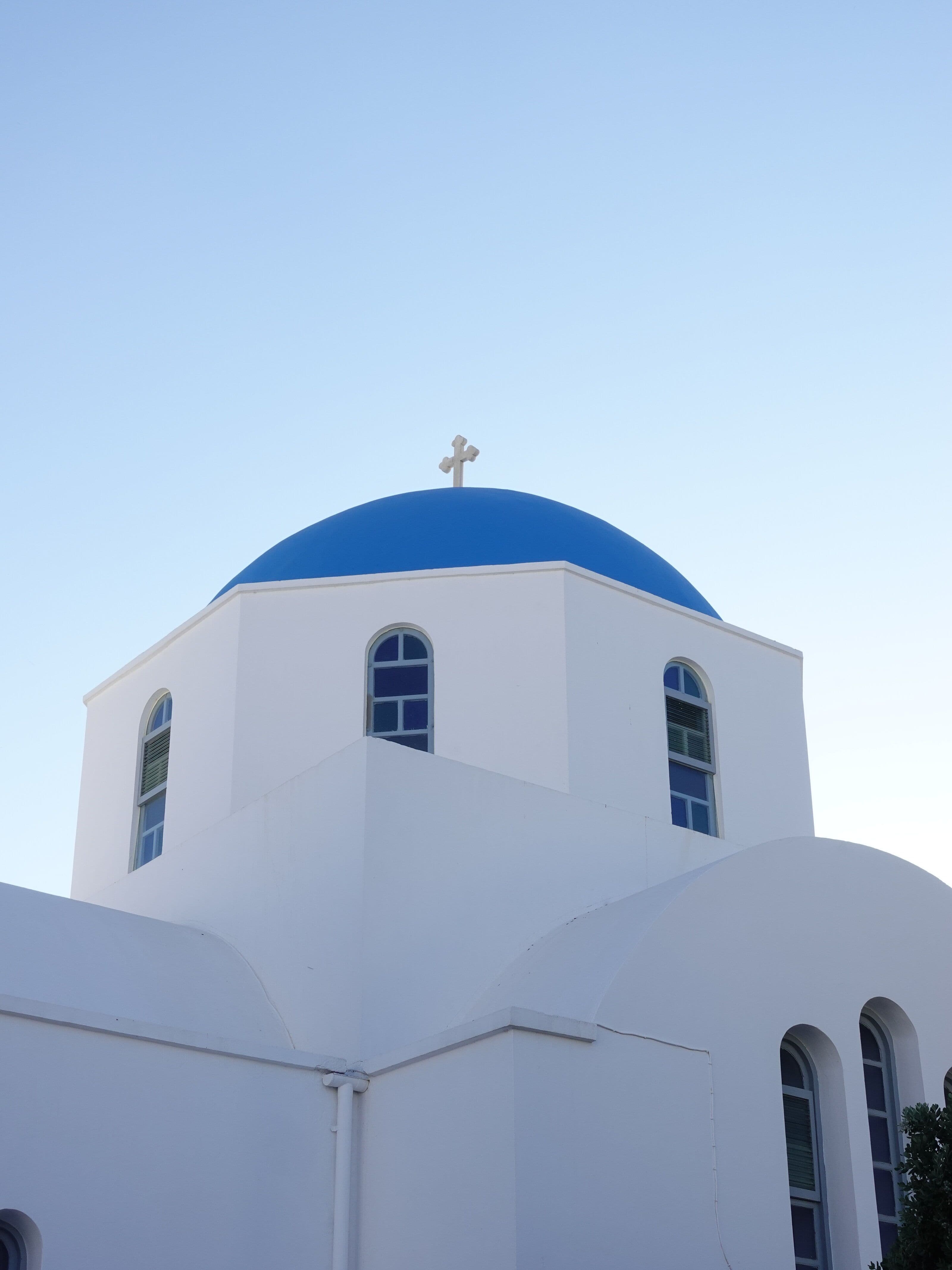 White Greek Orthodox church with a vivid blue dome and cross on top against a clear sky