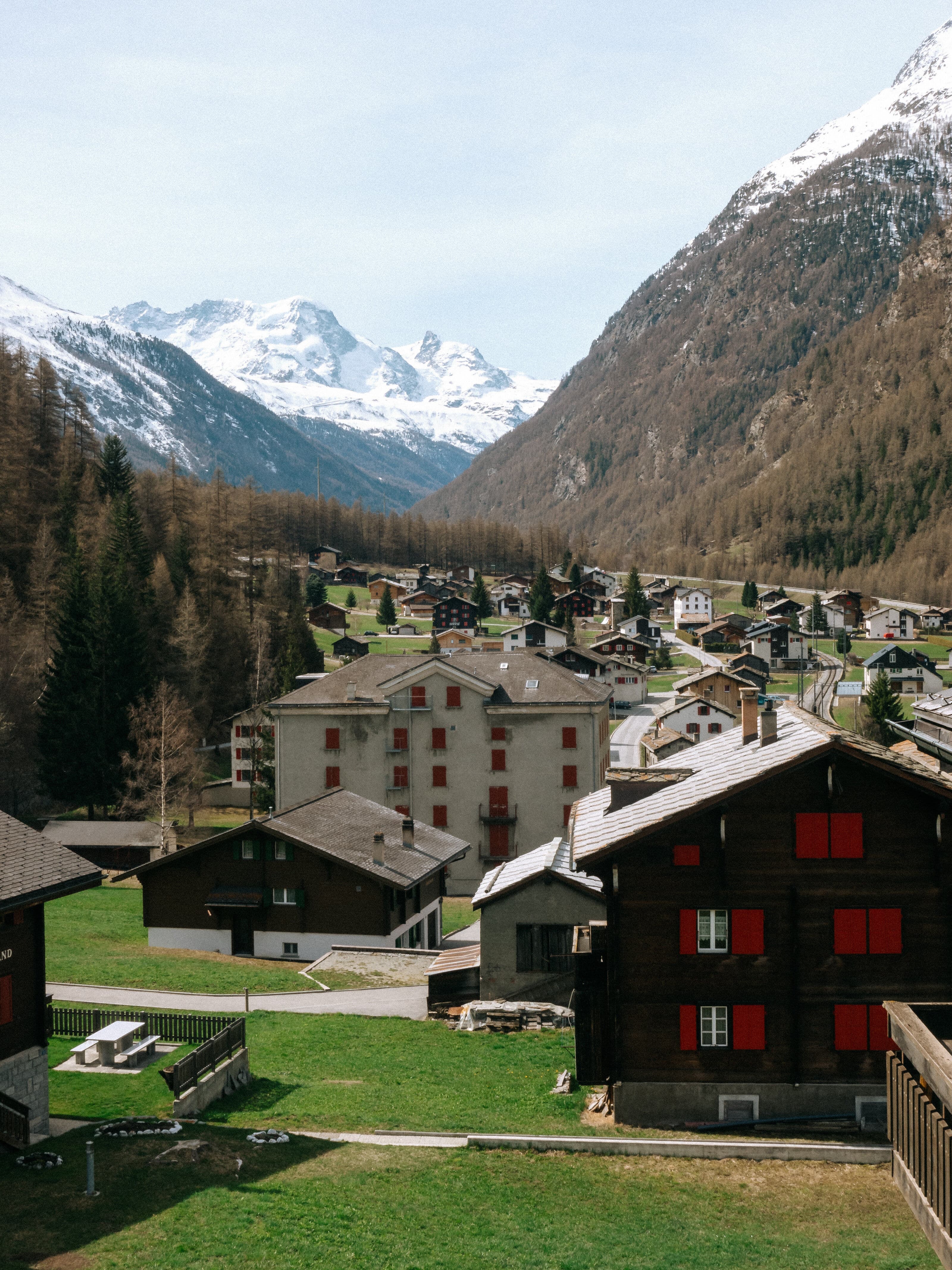 A Swiss alpine village with traditional wooden chalets and red shutters nestled in a valley beneath snow-capped mountain peaks